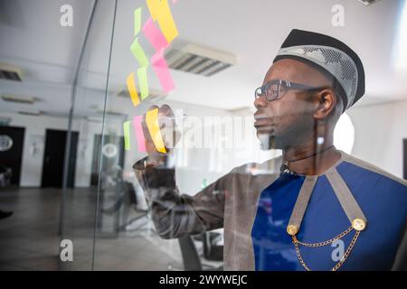 An African businessman writes on colorful sticky notes hanging on the wall in the office Stock Photo
