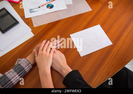 Business women make a stack with their hands near a paper with 'Girl Power' written on it, female empowerment concept Stock Photo