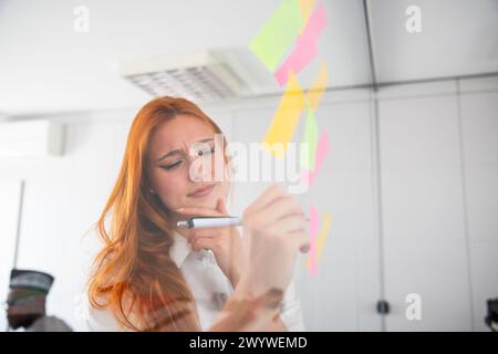Pensive businesswoman writes on sticky notes, brainstorming in the office Stock Photo