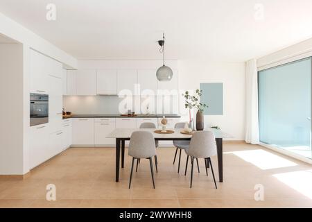 interior of modern furnished flat with open kitchen and large dining room. A table with four chairs and the sun coming in directly from the left. Stock Photo