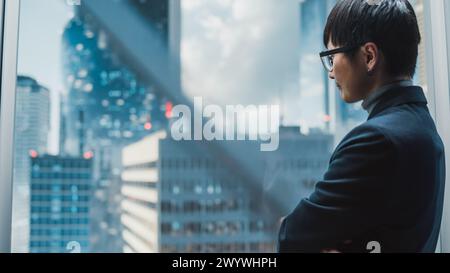 Stylish Japanese Businessman Riding Glass Elevator to Office in Modern Business Center in the Down Town. Young Sucessful Asian Male Interacting With Mock Up Holographic Screen in the Lift Concept. Stock Photo