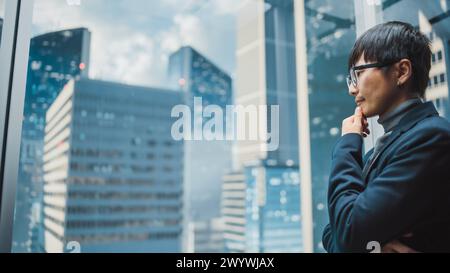 Stylish Japanese Businessman Riding Glass Elevator to Office in Modern Business Center in the Down Town. Young Sucessful Asian Male Interacting With Mock Up Holographic Screen in the Lift Concept. Stock Photo
