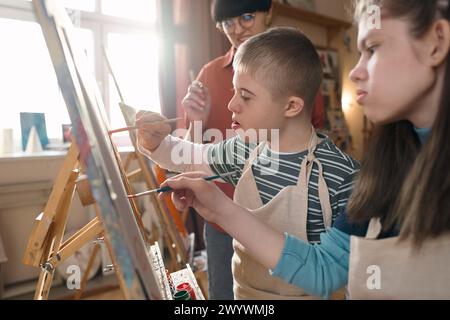 Portrait of two children with disability painting on easels in art ...