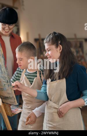 Vertical portrait of boy and girl with disability painting together on easel and smiling while enjoying art class Stock Photo