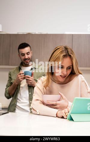 Happy carefree couple planing together with tablet and at home. Smiling man talking with woman using online device in the kitchen. Stock Photo