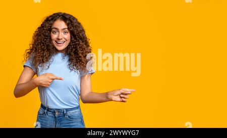 Woman pointing and looking surprised on yellow Stock Photo