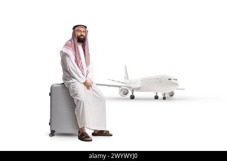 Saudi arab man sitting on a suitcase at the airport and waiting for a plane isolated on white background, Stock Photo