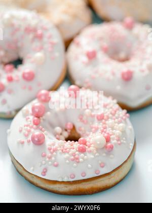 Delicious tender donuts glazed white glaze and sprinkled with pink pearl dressing. Idea decorating donuts for wedding, romantic event, celebration. Selective focus with copy space. Vertical Stock Photo