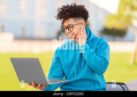 Man using phone and laptop simultaneously, studying at park Stock Photo