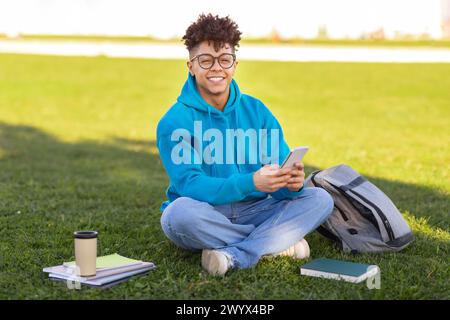 Student sitting on grass with smartphone, studying at park Stock Photo