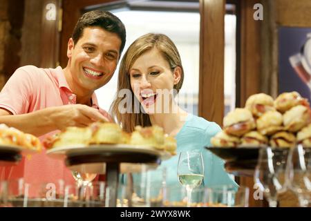 Couple drinking wine and eating tapas. Pintxos. Bar txondorra. Parte Vieja. Old town. San Sebastian. Donostia. Gipuzkoa. Basque Country. Spain. Stock Photo