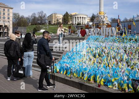 April 5, 2024, Kyiv, Ukraine: A man on crutches smokes near an improvised memorial site on Independence Square in Kyiv, where relatives and friends plant Ukrainian flags with the names of military personnel killed in battles with the Russian army. Ukrainian capital is located away from the fighting places, but the presence of war is felt in the city and affects many aspects of the life of local residents. Russian troops entered Ukrainian territory on February 2022, starting a conflict that provoked the destruction of areas and humanitarian crisis. (Credit Image: © Oleksii Chumachenko/SOPA Imag Stock Photo