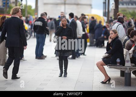 Girl sitting on a bench and calling while another is standing in front of her in Paris France, other people walking  on the champs Elysees in summer 2 Stock Photo