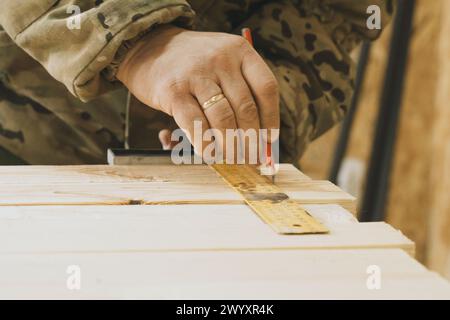 A close-up view of a carpenters hands using a pencil and ruler to mark precise measurements on a wooden board during a woodworking project. Stock Photo