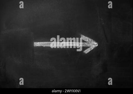 White arrow hand painted with chalk on a black blackboard indicating the direction Stock Photo