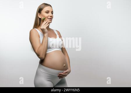 Pretty pregnant young woman with a face roller in hands Stock Photo