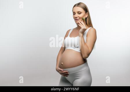 Pretty pregnant young woman with a face roller in hands Stock Photo