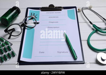 Clipboard with medical prescription form, stethoscope, pills and glasses on white wooden table Stock Photo