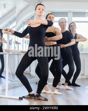 Woman practicing demi plie at barre during group ballet class Stock Photo