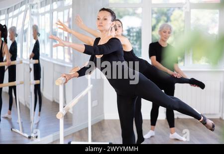Woman performing arabesque at barre during group ballet class Stock Photo
