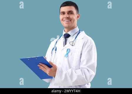 Male urologist with blue ribbon writing in clipboard on color background. Prostate cancer awareness concept Stock Photo