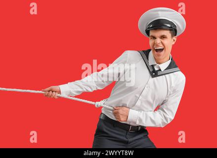 Angry young sailor pulling rope on red background Stock Photo