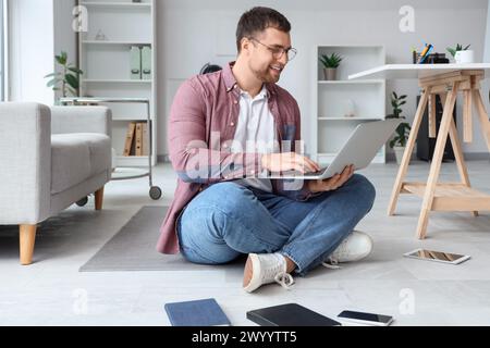 Male programmer with laptop and different gadgets sitting on floor in office Stock Photo