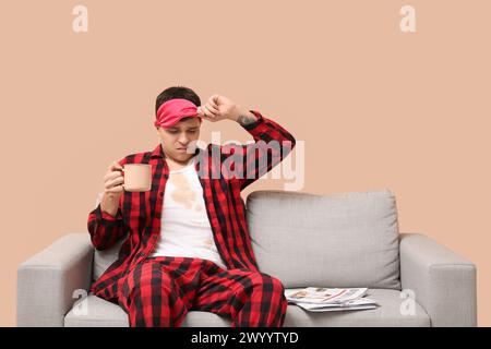 Stressed young man with coffee stains on his pajamas and newspaper on beige background Stock Photo