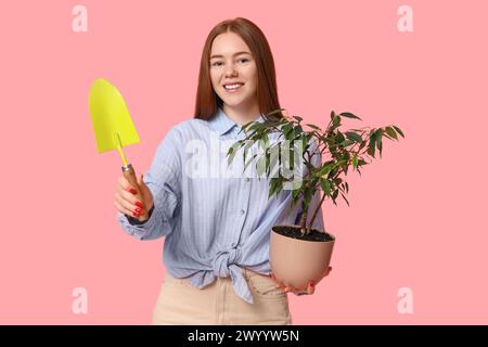 Pretty young woman with houseplant and gardening tool on pink background Stock Photo
