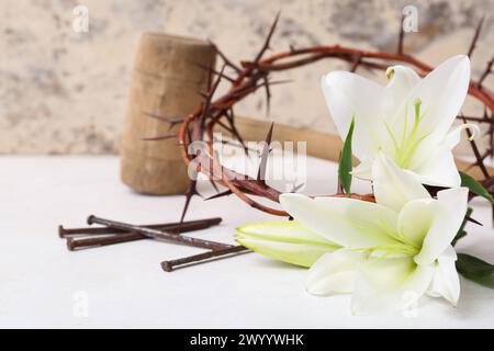 Composition crown of thorns, lilies, nails and hammer on white table near light wall Stock Photo