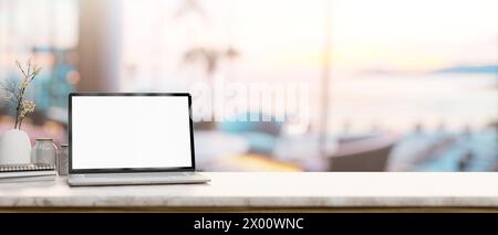 A white-screen laptop computer mockup on a tabletop with a blurred background of a beachfront hotel lounge or restaurant. place of work concept. 3d re Stock Photo