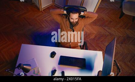 Top down view of IT admin in home office stretching after sitting on desk chair all day. Software engineer loosening up, relaxing after typing on computer for long period of time, aerial shot Stock Photo
