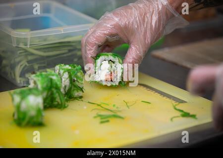A gloved hand cuts sushi on a cutting board. Stock Photo