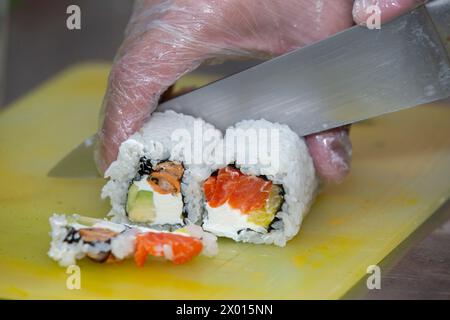 A gloved hand cuts sushi on a cutting board. Stock Photo