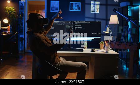 Self employed engineer using technologically advanced VR glasses in home office to do coding. Freelancing IT specialist wearing cutting edge virtual reality headset to visualize lines of code Stock Photo