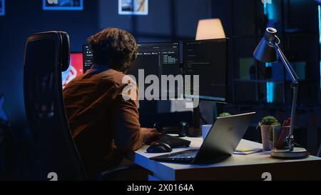Developer pressed by deadline, drinking coffee and doing multitasking to finish developing PC code. Caffeinated IT specialist solving database error using multiple desktop and laptop screens, camera A Stock Photo