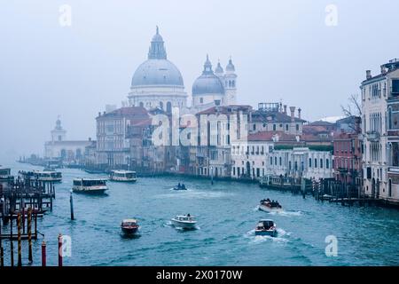 Canale Grande with Vaporettos and Basilica di Santa Maria della Salute, shrouded in mist, seen from the Ponte dell'Accademia bridge. Stock Photo