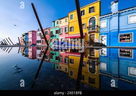 Colourfully painted houses along a water canal on the island of Burano, reflected in a puddle of water. Stock Photo