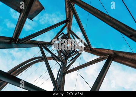 Electricity distribution tower from below, high voltage power lines under cloudy sky. Stock Photo