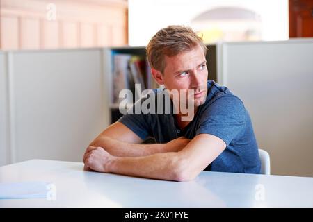 Man, looking away and upset with paper on table in workspace for stress, worry and thinking for job. Young person, contemplate or anxious mindset Stock Photo