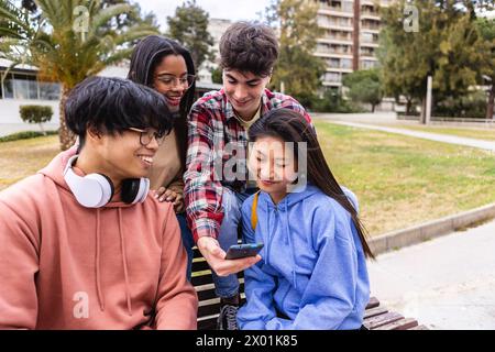 Happy student friends using mobile phone together sitting at college campus Stock Photo