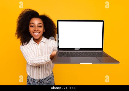 Young woman presenting laptop screen on yellow background Stock Photo