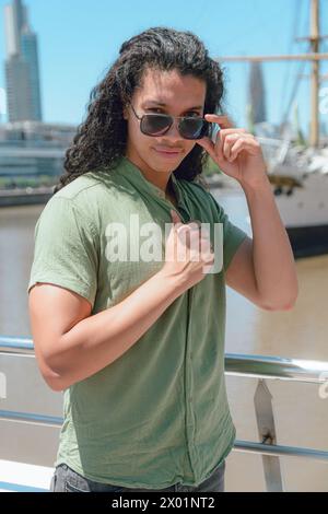 Vertical portrait of handsome young man with curlers and sunglasses, with strong body and sunglasses posing and watching camera standing on woman's br Stock Photo