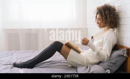 Young woman reading book and drinking coffee on bed Stock Photo