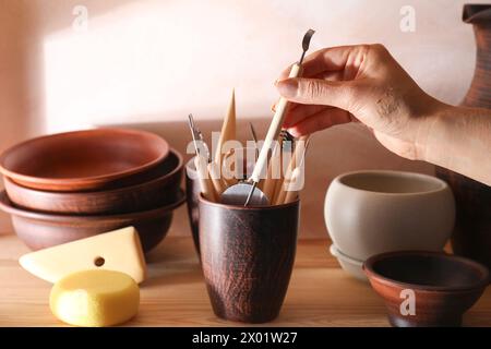 Woman taking clay crafting tool from cup in workshop, closeup Stock Photo