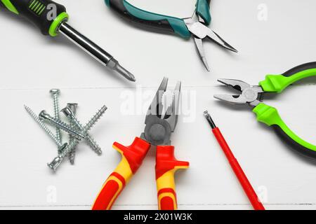 Pliers, screwdrivers and screws on white wooden table, flat lay Stock Photo