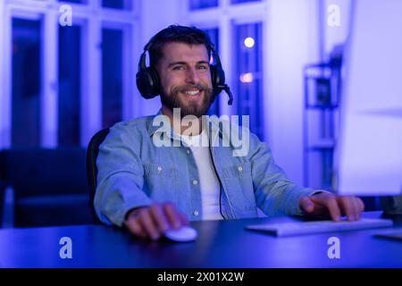 Smiling man using computer at night in neon light Stock Photo