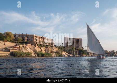ASWAN, EGYPT - SEPTEMBER 03, 2017: An Egyptian felucca or sailing boat on the Nile at Aswan with the famous Old Cataract Hotel on the shoreline. Stock Photo