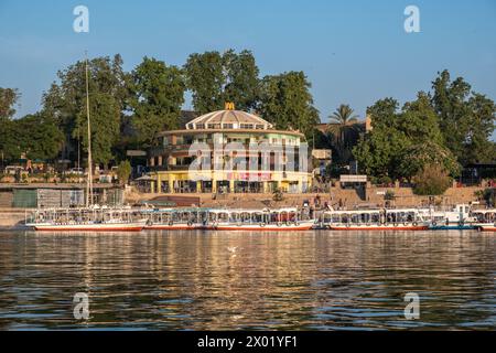 ASWAN, EGYPT - SEPTEMBER 03, 2017: Tourist boats on the Nile at Aswan with a circular McDonald's fast food restaurant on the shore. Stock Photo