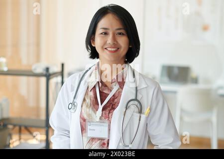 Portrait of smiling general practitioner in white coat standing in her office Stock Photo